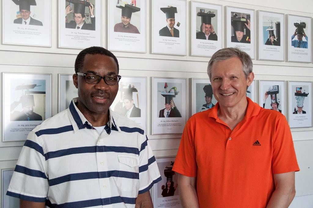 Prof Bobda and Prof. Teich in front of pictures of graduates