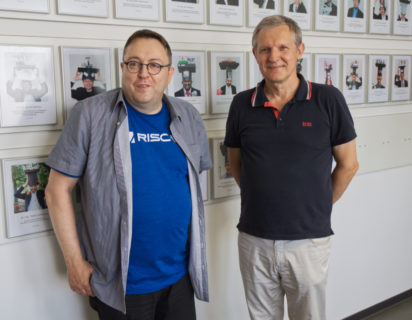 Two persons standing in front of a wall with pictures on it