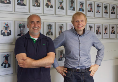 Two men standing in front of a wall with pictures on it