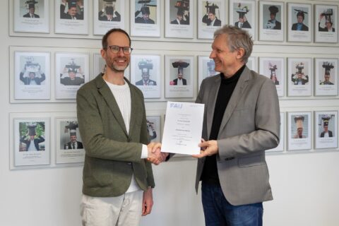 2 men in front of picture wall handing over a certificate