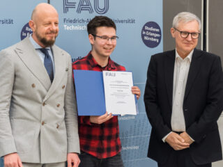 Three people, the middle one holding an award in his hand