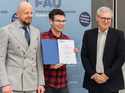 Three people, the middle one holding an award in his hand