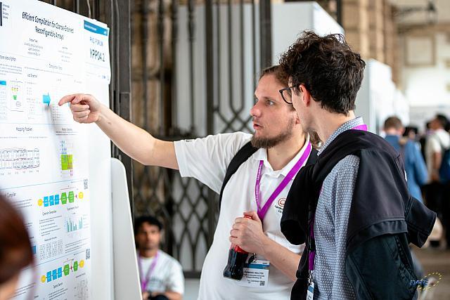 Two men standing in front of a poster, while one is explaining something to the other