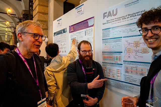 Multiple men standing in front of posters while one is smiling directrly into the camera.
