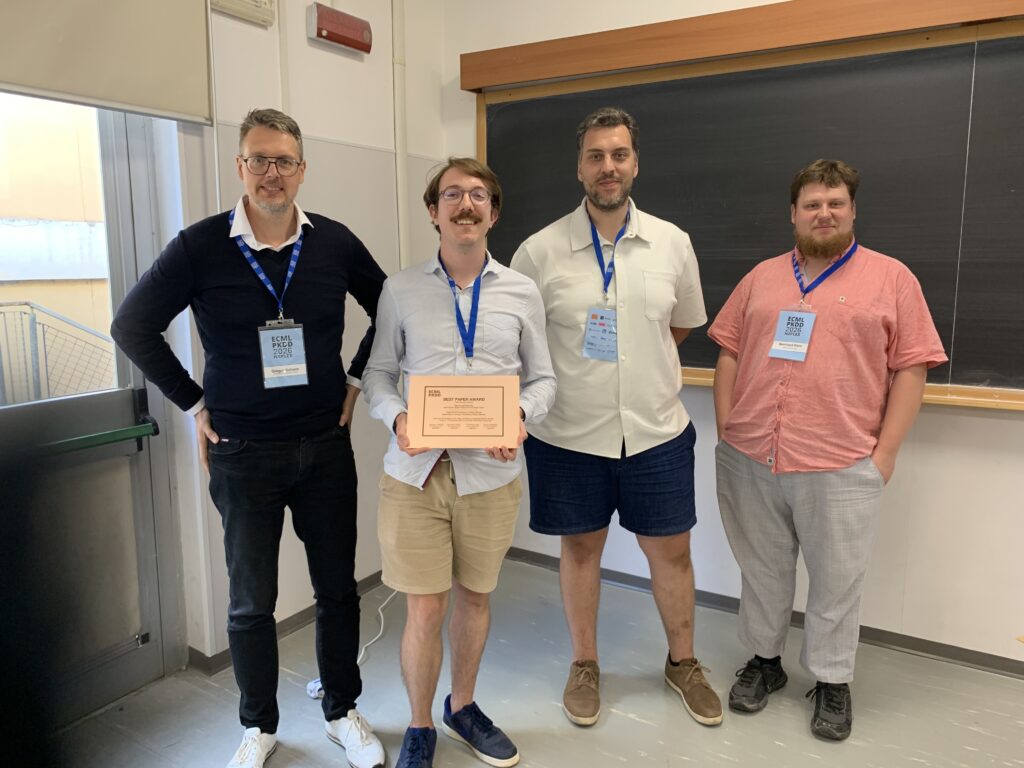 Four men standing in front of a blackboard. One of them is holding an award.